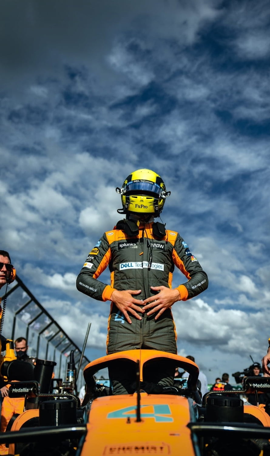 Lando Norris standing on his McLaren Formula 1 car under a dramatic cloudy sky HD phone wallpaper