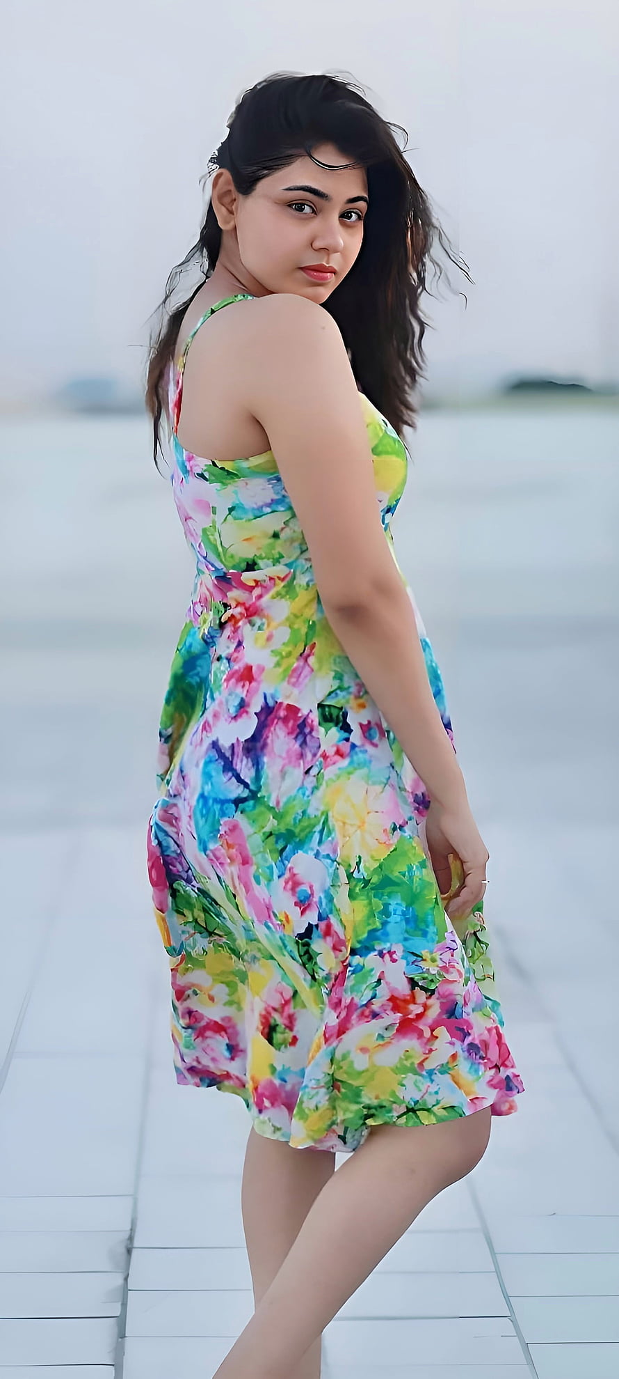 Young woman in a vibrant floral summer dress standing on a white tiled walkway HD phone wallpaper