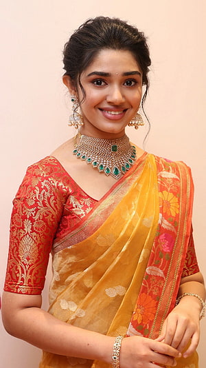 Krithi Shetty in a vibrant red and gold silk saree with traditional emerald jewelry HD phone wallpaper