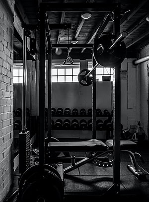 Monochrome View of a Weightlifting Rack and Dumbbell Racks in a Brick-Walled Gym HD phone wallpaper