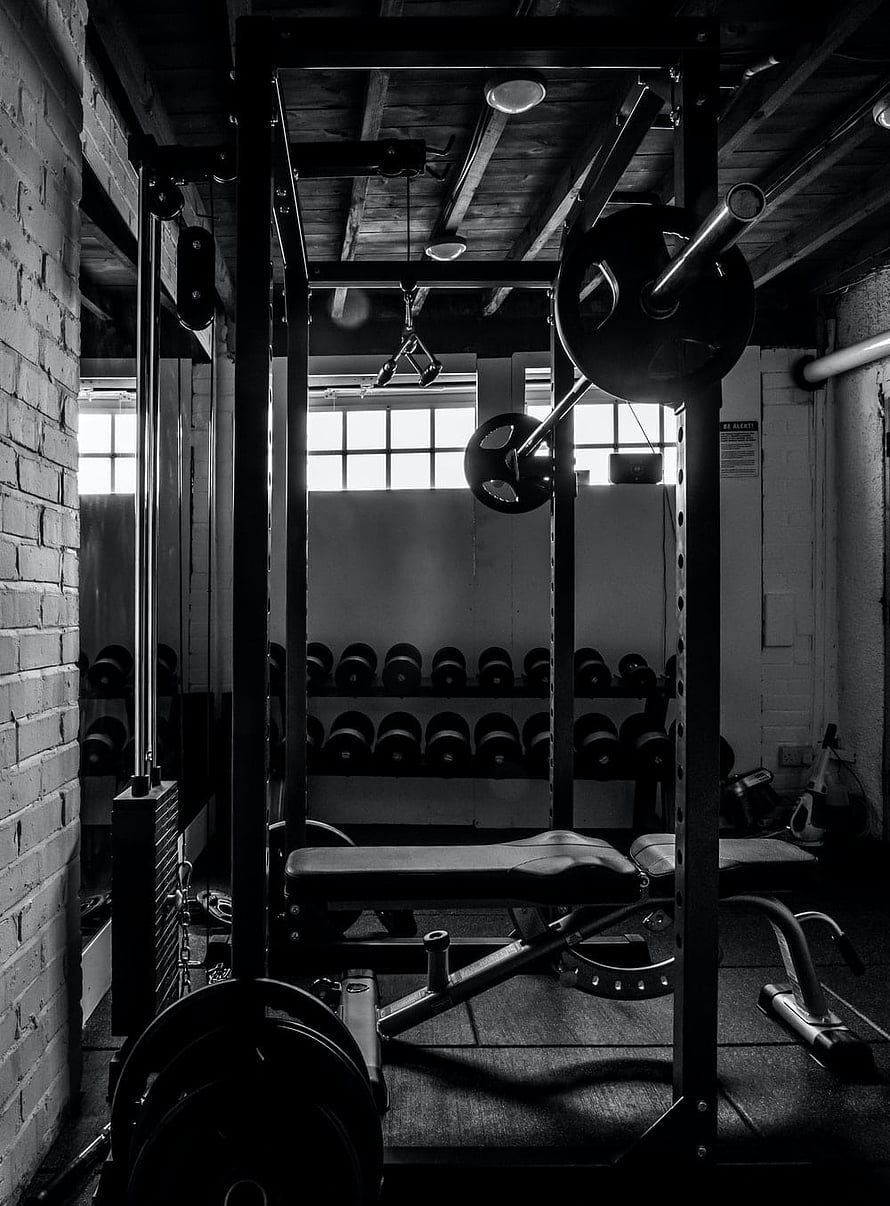 Monochrome View of a Weightlifting Rack and Dumbbell Racks in a Brick-Walled Gym HD phone wallpaper