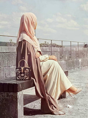Elegant Hijabi Woman in Pastel Abaya and Blouse Sitting on a Bench with Ornate Handbag HD phone wallpaper