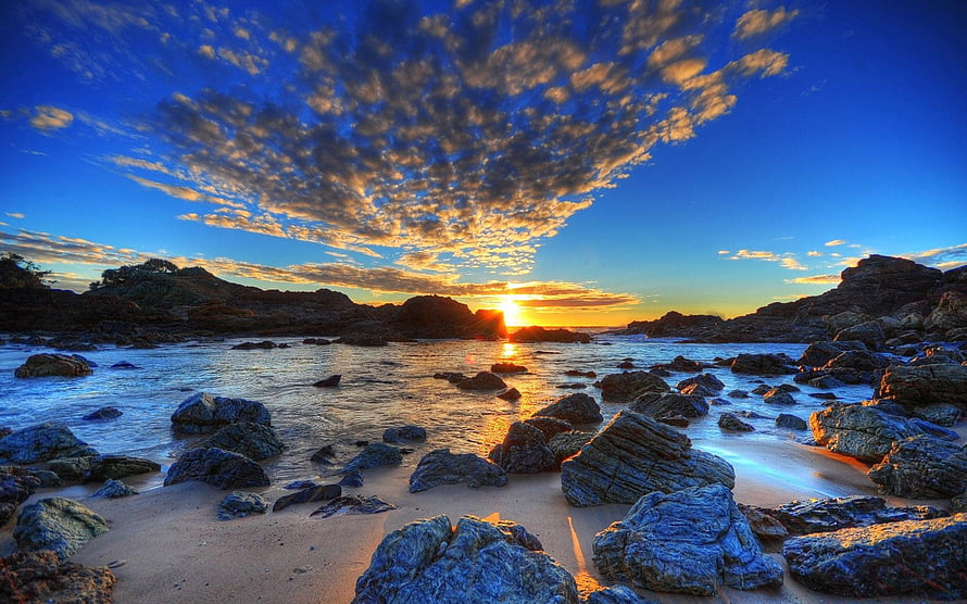 Golden sunset over a rocky shoreline with dramatic clouds and calm sea HD wallpaper