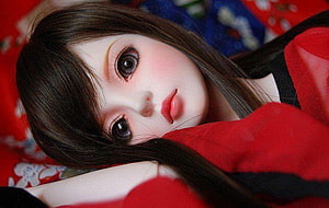 Close-up of a realistic ball-jointed doll with long dark hair resting on a red patterned blanket HD wallpaper