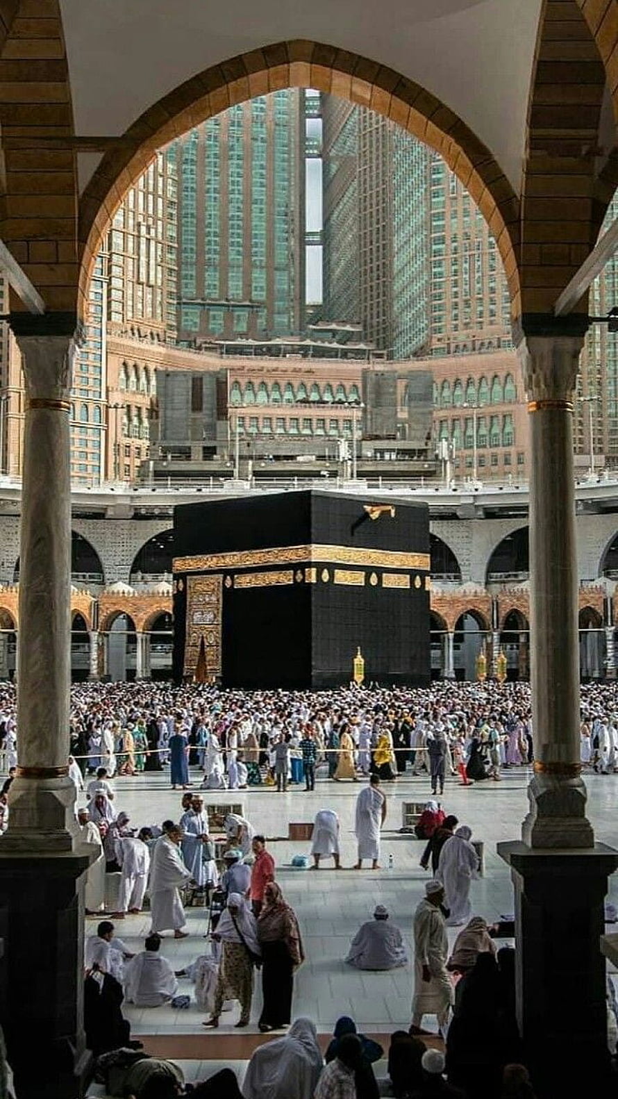 Pilgrims gathered around the Kaaba in Makkah framed by a grand stone archway HD phone wallpaper