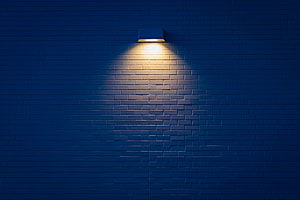 Warm Sconce Light Casting a Glow on a Dark Blue Brick Wall at Night HD wallpaper
