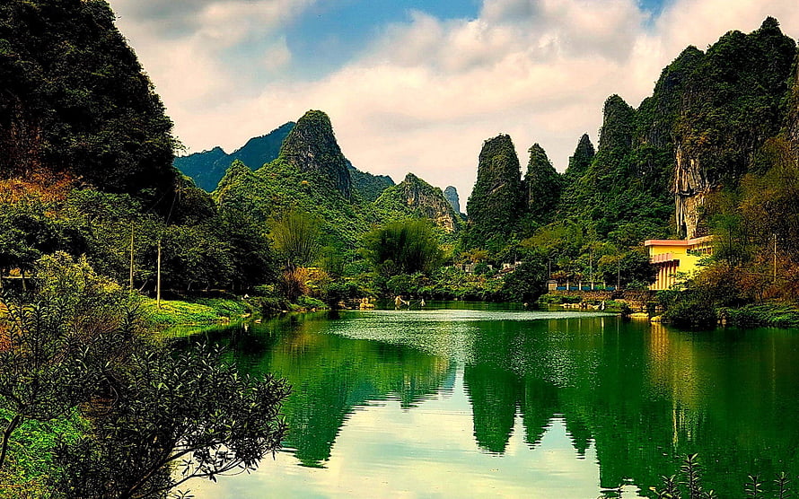 Serene Karst Mountain Lake Landscape with Lush Green Reflections and Dramatic Cloudy Sky HD wallpaper