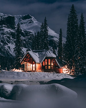 Cozy Snow-Covered Mountain Lodge at Night with Warm Interior Lighting HD phone wallpaper