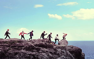 BTS Members Walking Along Rocky Coastal Cliffs Under a Bright Blue Sky HD wallpaper