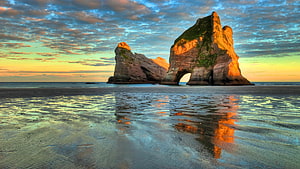 Dramatic Coastal Rock Arch at Golden Hour with Mirror-Like Beach Reflections HD wallpaper