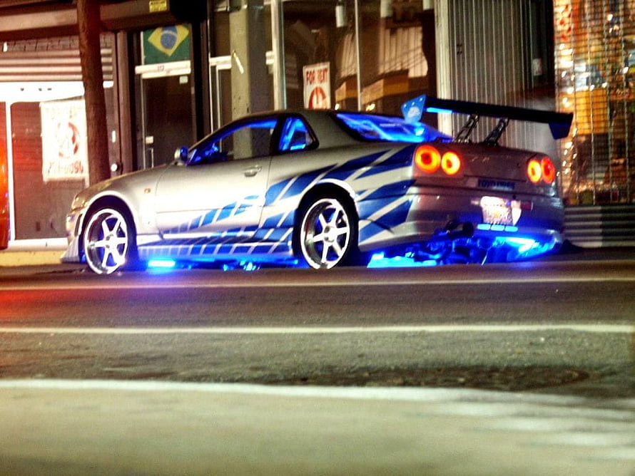 Nissan Skyline GT-R R34 with Blue Underglow and Custom Livery Parked on a City Street at Night HD wallpaper