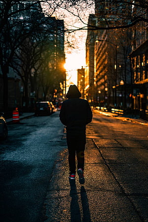 Silhouette of a man walking down a city street at golden hour with long shadows HD phone wallpaper