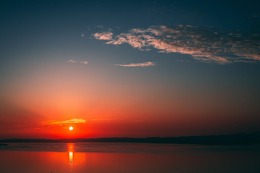 Vibrant sunset over a calm sea with a glowing horizon and scattered clouds HD wallpaper