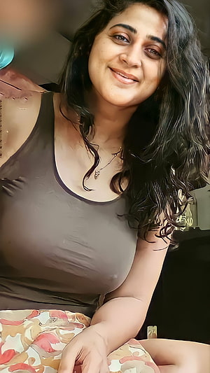 Portrait of a smiling woman with long dark wavy hair wearing a grey tank top and floral skirt HD phone wallpaper