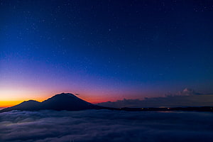 Volcanic Peak Rising Above Sea of Clouds Under a Starry Twilight Sky HD wallpaper