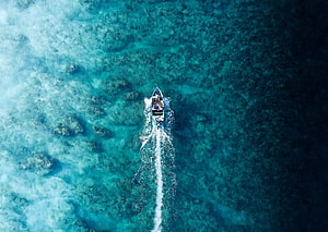 Aerial view of a speedboat cutting through turquoise coral reef waters HD wallpaper