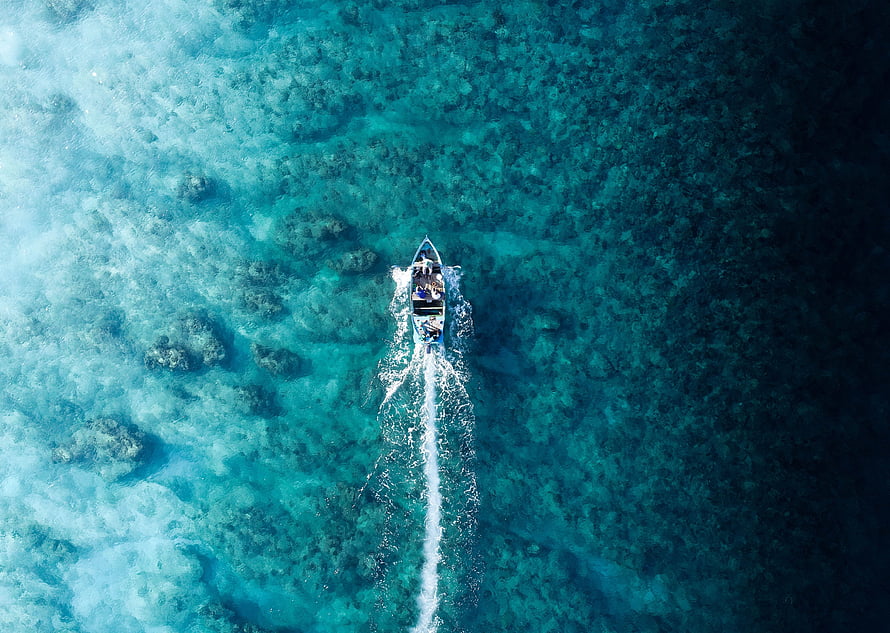 Aerial view of a speedboat cutting through turquoise coral reef waters HD wallpaper