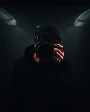 Mysterious Photographer in Black Beanie Holding Camera in Dim Studio Lighting HD phone wallpaper