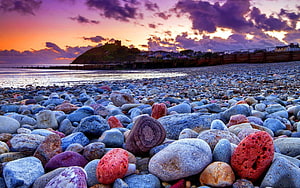Colorful pebble beach at sunset with dramatic purple clouds and coastal cliffs HD wallpaper