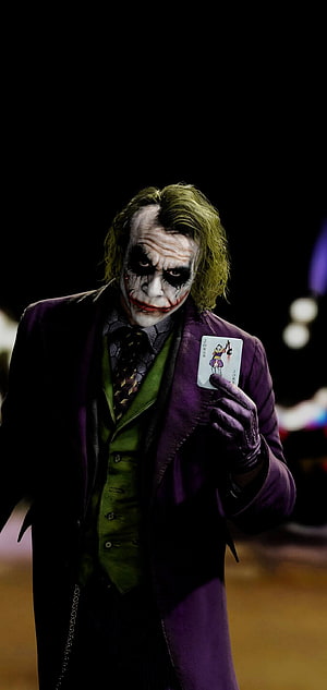 Joker in purple suit holding playing card against dark background HD phone wallpaper