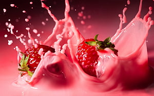 Strawberries splashing in pink liquid with dynamic droplets and vibrant red tones HD wallpaper