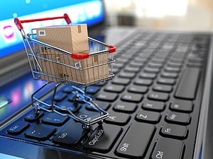 Miniature shopping cart with cardboard boxes on a laptop keyboard representing online retail HD wallpaper