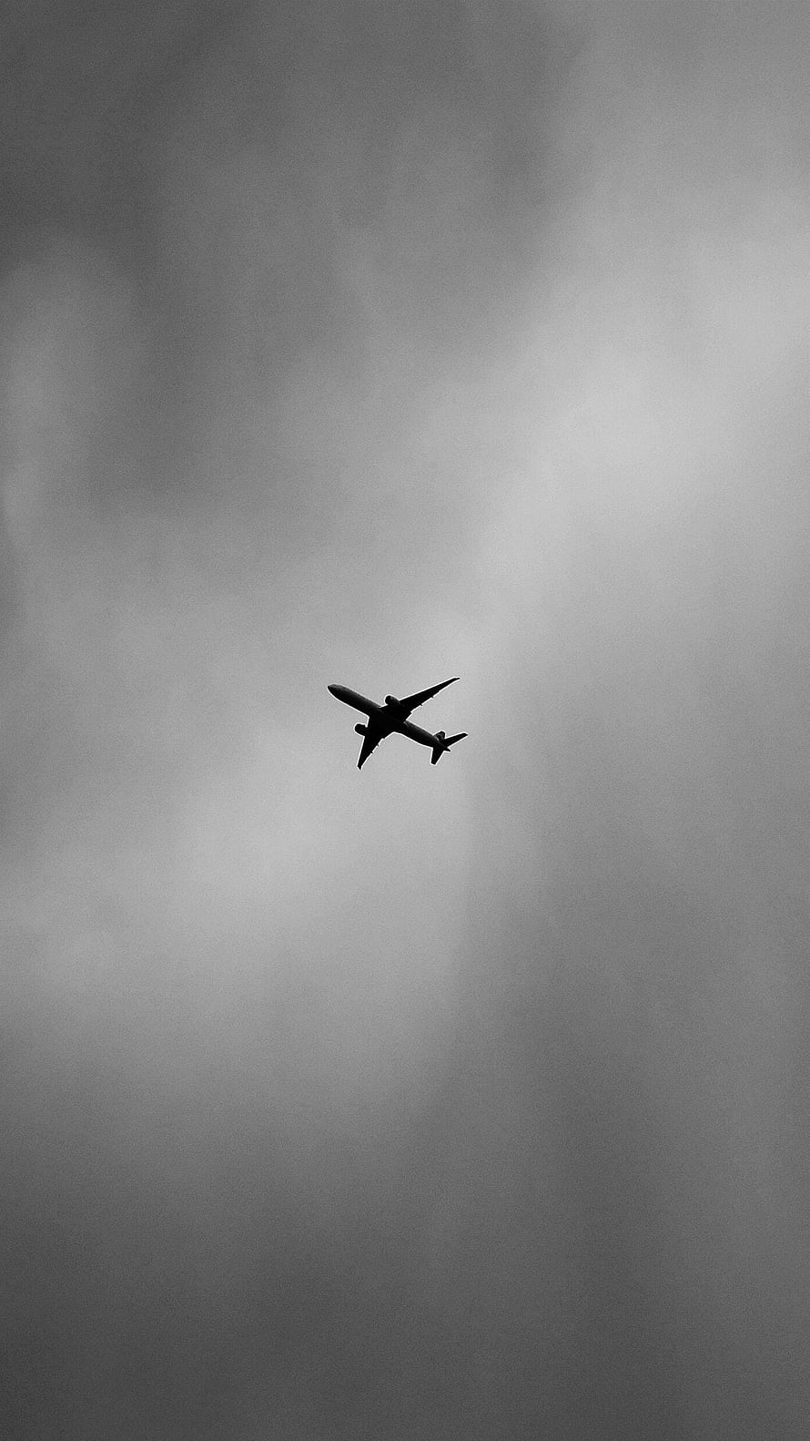 Black and White Airplane Silhouette Soaring Through Moody Overcast Clouds HD phone wallpaper