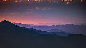 Layered Mountain Ranges Under a Soft Pink and Purple Dawn Sky HD wallpaper