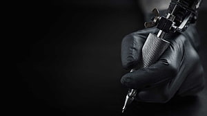 Close-up of a gloved hand holding a professional tattoo machine against a dark background HD wallpaper