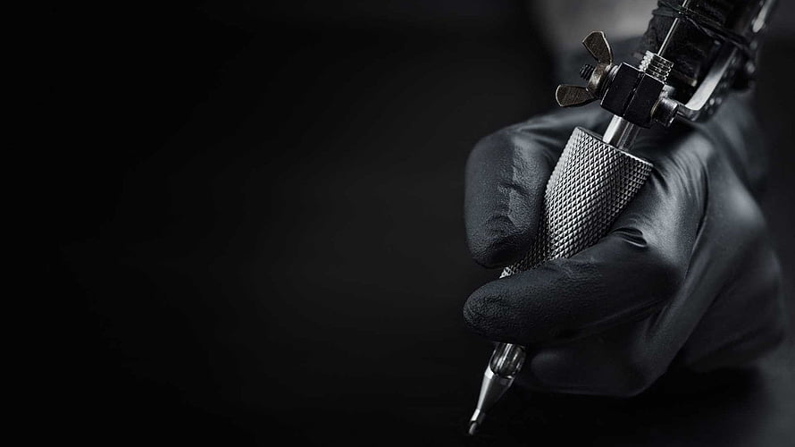 Close-up of a gloved hand holding a professional tattoo machine against a dark background HD wallpaper