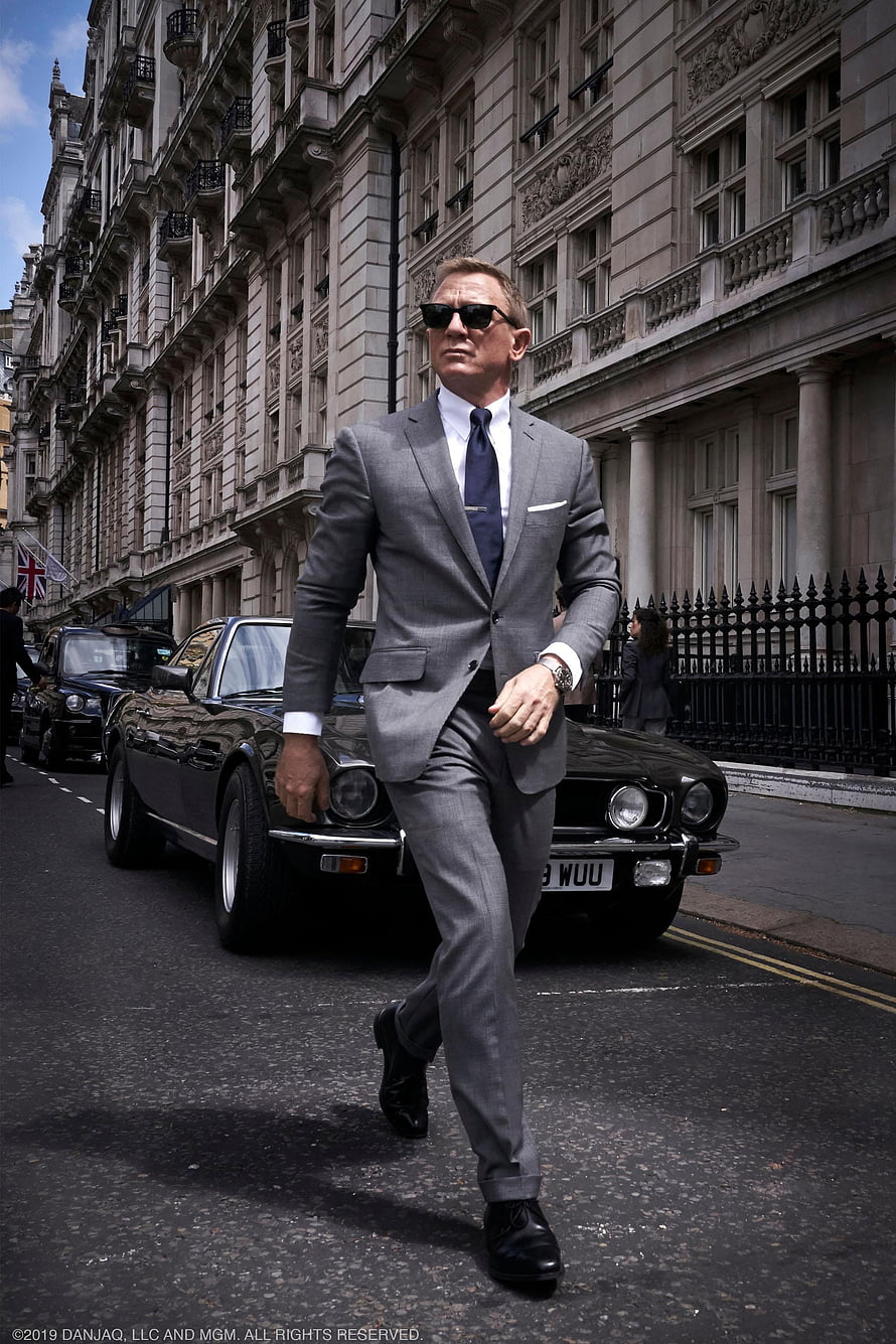 Daniel Craig as James Bond in a grey suit walking past a classic Aston Martin in London HD phone wallpaper