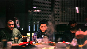 The Weeknd seated at a dimly lit table with two companions in a moody urban setting HD wallpaper