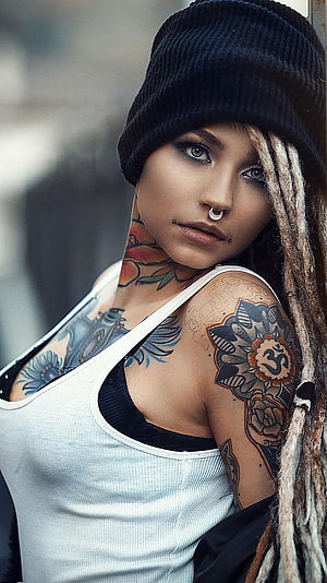 Portrait of a woman with dreadlocks, beanie, and colorful floral and mandala tattoos on her neck and arm HD phone wallpaper