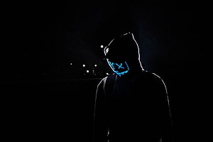 Silhouetted figure in a hood wearing a glowing blue LED mask in a dark night setting HD wallpaper
