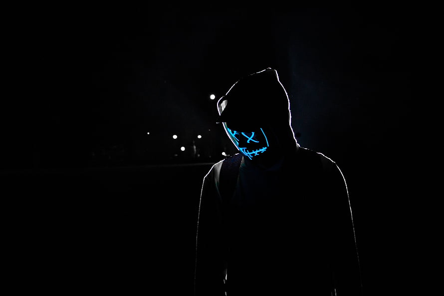 Silhouetted figure in a hood wearing a glowing blue LED mask in a dark night setting HD wallpaper