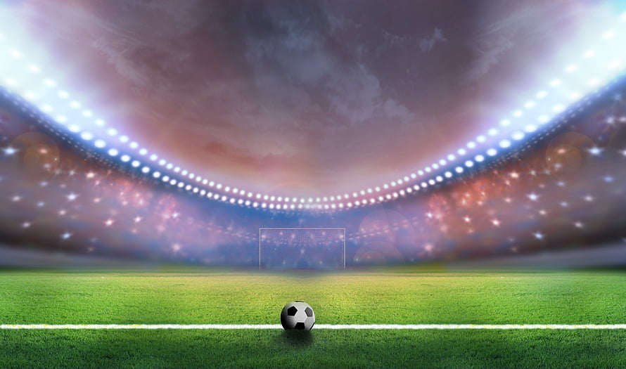 Soccer ball on a green pitch under bright stadium floodlights with a dramatic cloudy sky HD wallpaper