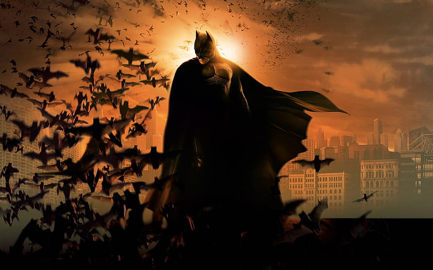 Batman Silhouette Standing Before a Swarm of Bats Against a Dramatic Orange Sky HD wallpaper