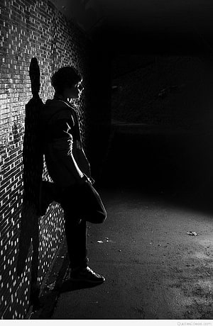 Moody Black and White Portrait of a Young Man Leaning Against a Brick Wall in a Dark Alley HD phone wallpaper