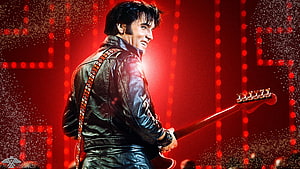 Elvis Presley performing on stage in a black leather jacket with electric guitar under red lights HD wallpaper