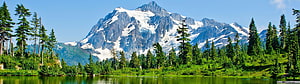 Snow-Capped Mountain Peak Rising Over a Calm Alpine Lake and Evergreen Forest HD wallpaper