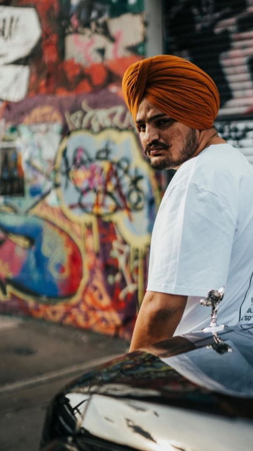 Sidhu Moose Wala in Orange Turban Leaning on Car Against Vibrant Graffiti Wall HD phone wallpaper