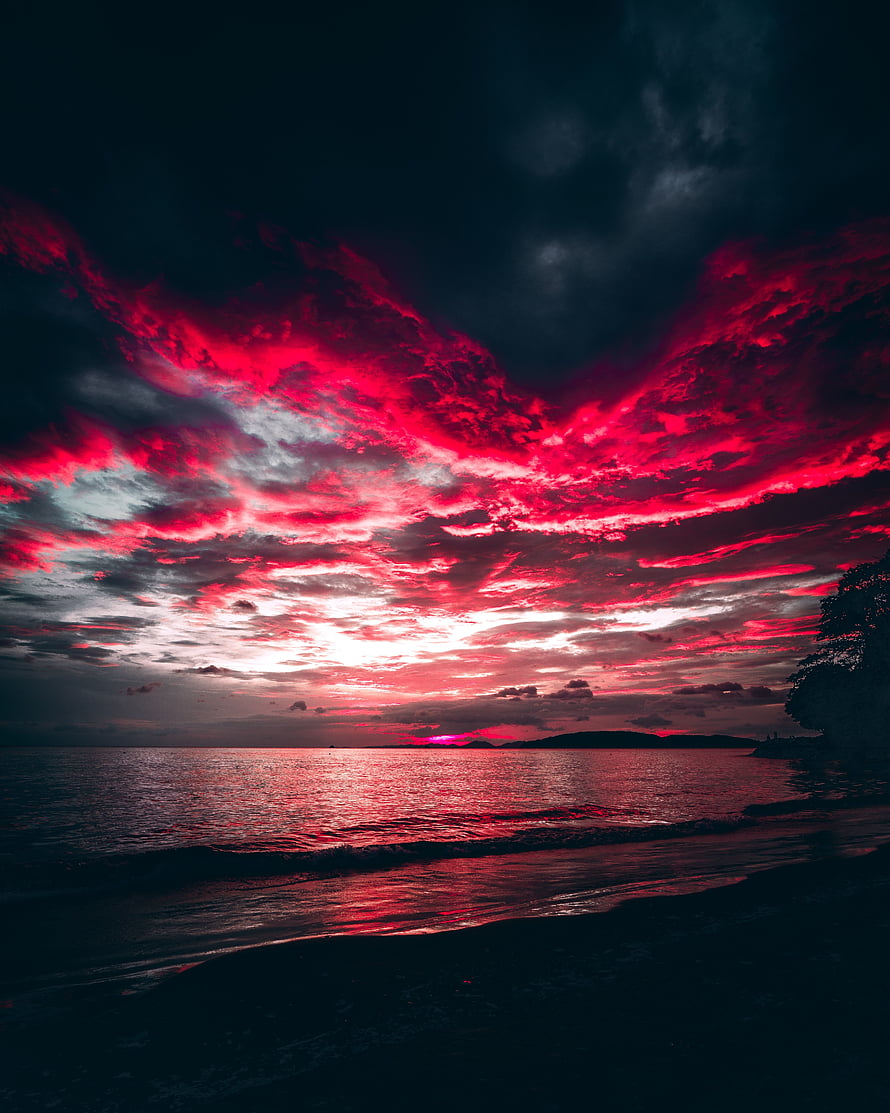 Crimson Sunset Over the Ocean with Dramatic Red Clouds and Dark Beach Silhouette HD phone wallpaper