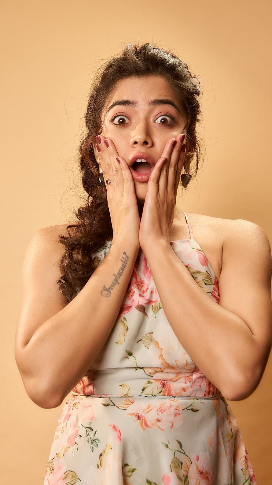 Rashmika Mandanna in a floral dress with a surprised expression and hands on her face HD phone wallpaper