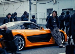 Tony Takahashi Leaning Against Orange Mazda RX-7 in Tokyo Drift Scene HD wallpaper