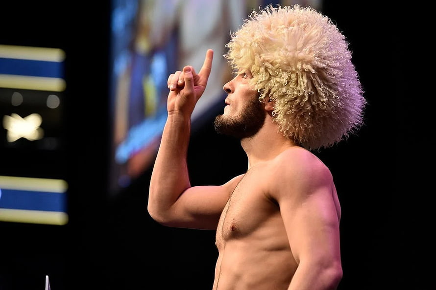 Khabib Nurmagomedov in a curly blonde wig pointing upward during a UFC event HD wallpaper