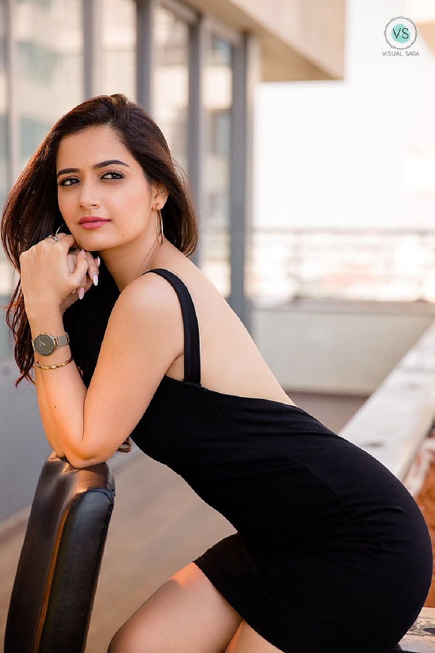 Ashika Ranganath in a Black Dress Leaning on a Chair in an Urban Setting HD phone wallpaper