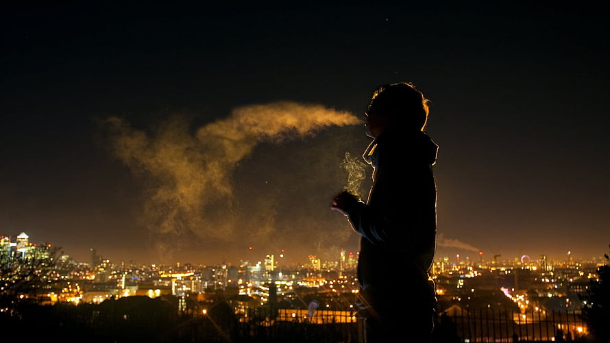 Silhouette of a Man Smoking Against a Glowing City Skyline at Night HD wallpaper