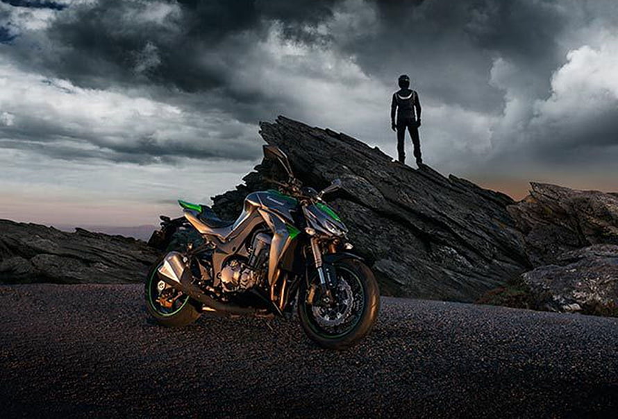 Kawasaki Z1000 sport bike parked on rocky terrain under dramatic storm clouds HD wallpaper