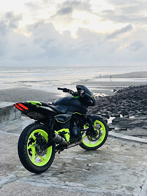 Modified Bajaj Pulsar 180 with neon green wheels parked on a coastal concrete platform at dusk HD phone wallpaper