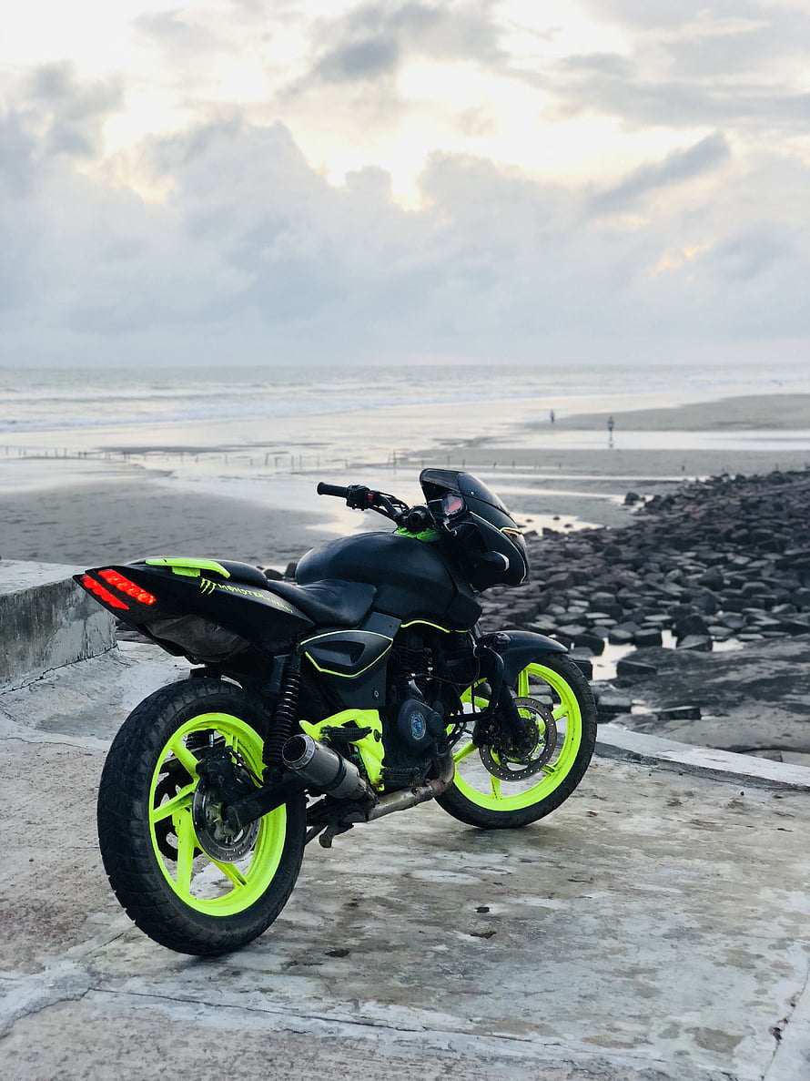 Modified Bajaj Pulsar 180 with neon green wheels parked on a coastal concrete platform at dusk HD phone wallpaper